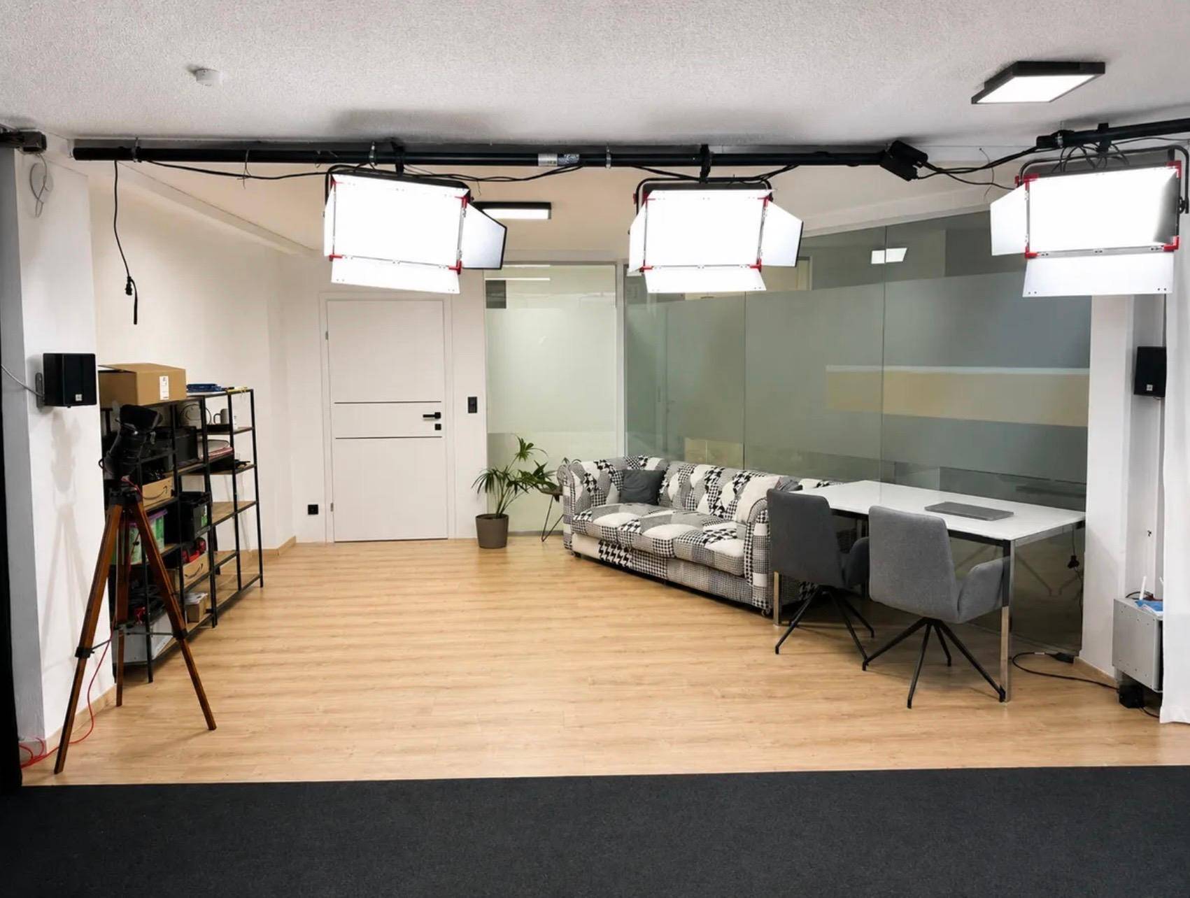 Geräumiger Studiobereich mit professioneller Beleuchtung, einem Sofa und hellem Laminatboden.