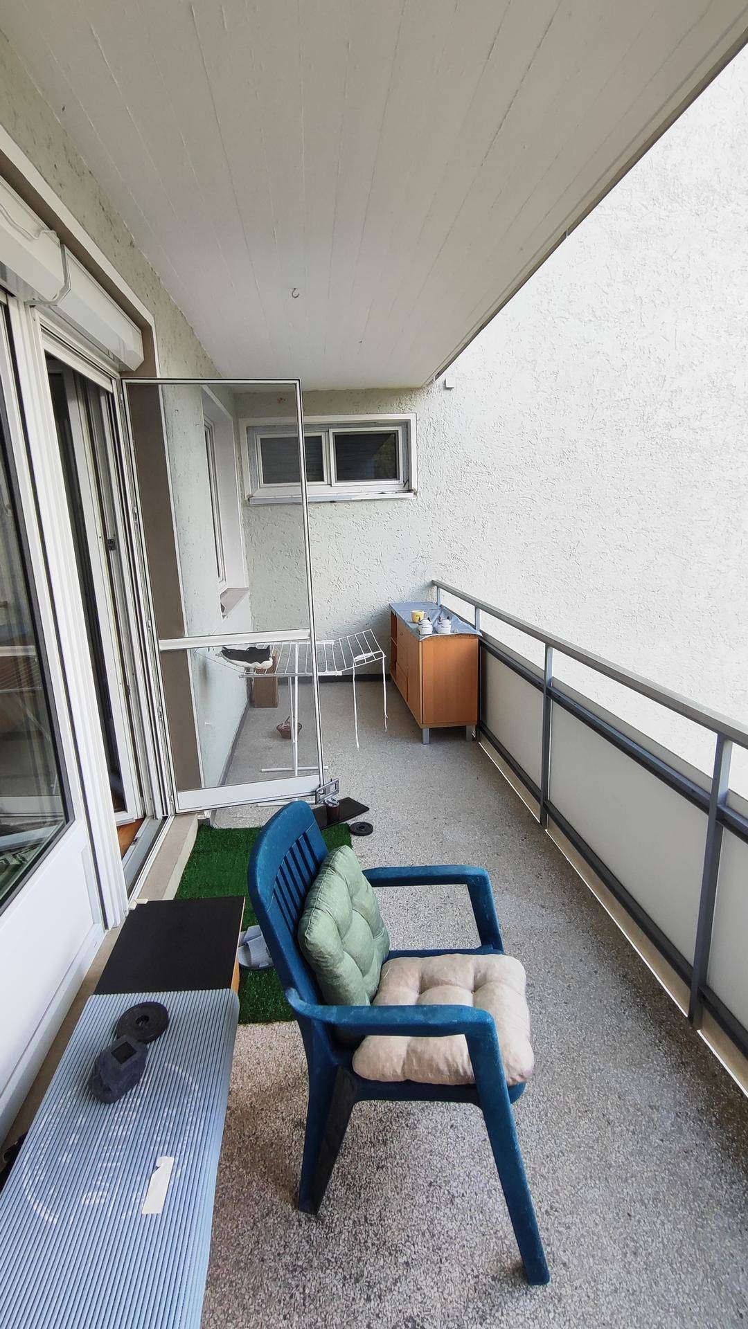 Schmaler Balkon mit blauen Gartenstühlen und Blick auf die Umgebung.