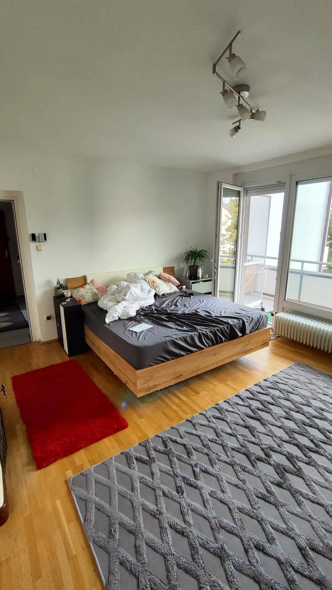 Schlafzimmer mit Holzbett, Parkettboden und Zugang zu einem Balkon.
