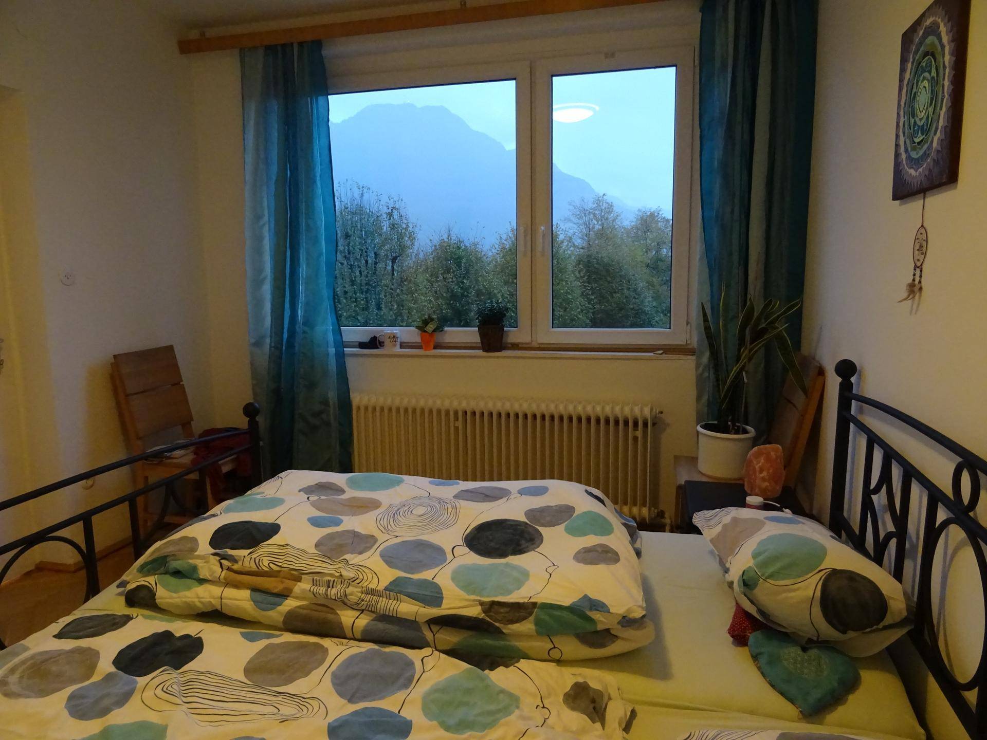 Schlafzimmer mit Doppelbett, blauen Vorhängen und Blick auf die Berge.