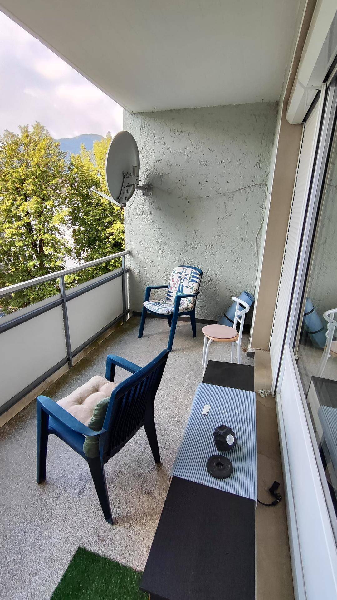 Balkon mit Gartenmöbeln, Satellitenschüssel und Blick auf Bäume und Berge.