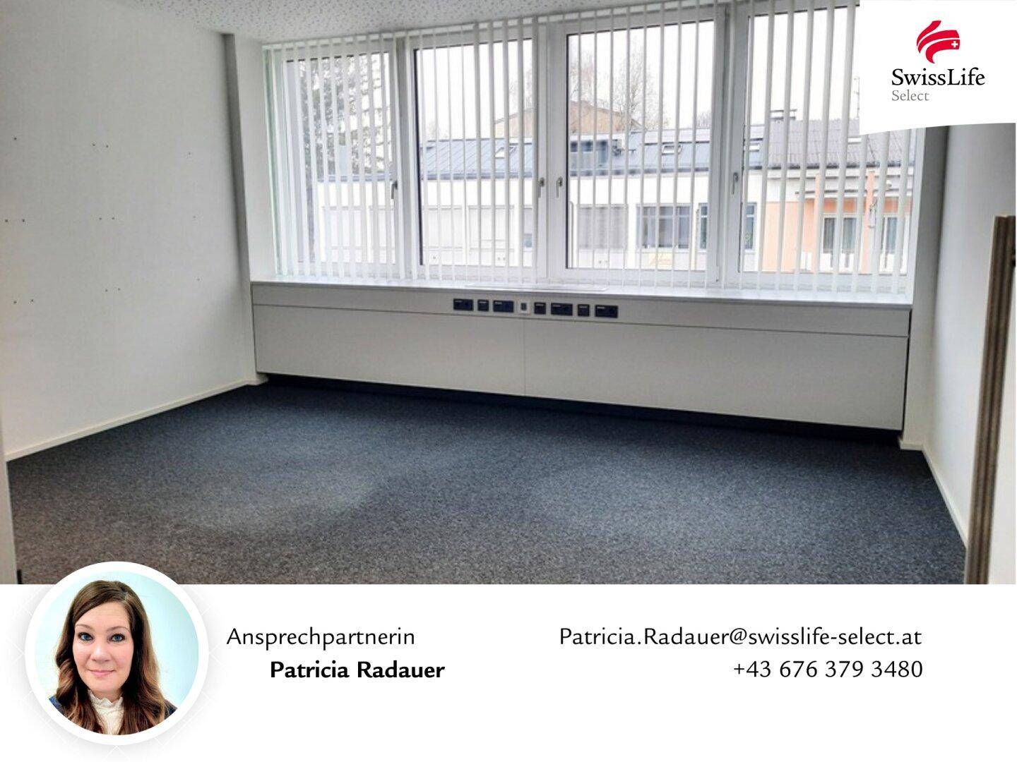 Leeres Büro mit großen Fenstern, vertikalen Jalousien und einem niedrigen Schrank unter den Fenstern.