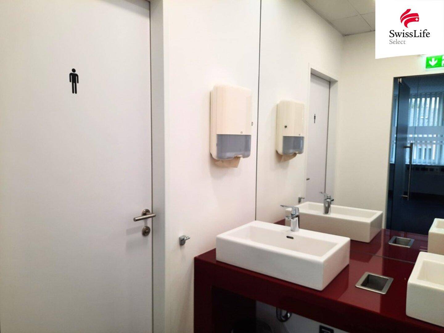 Herren-WC mit modernem, rechteckigem Waschbecken, großem Spiegel und weißer Tür mit Männchen-Symbol.