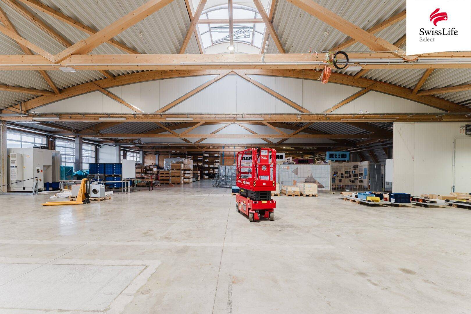 Geräumige Lagerhalle mit hoher Decke, Holzbalkenkonstruktion und Betonboden, bereit für die Nutzung.