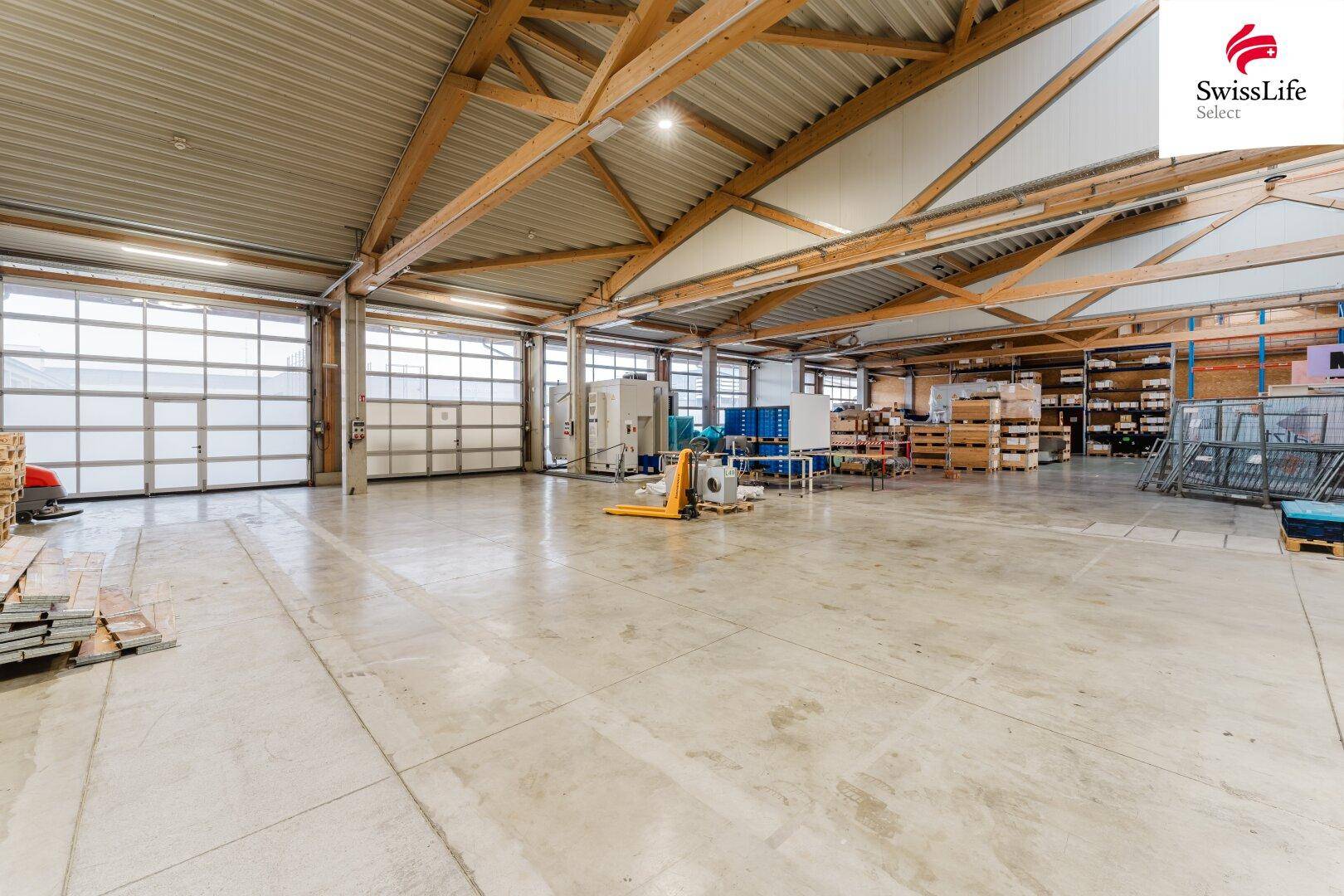 Große Lagerhalle mit Rolltoren, Betonboden und Holzbalken, bietet viel Platz für Logistik und Lagerung.