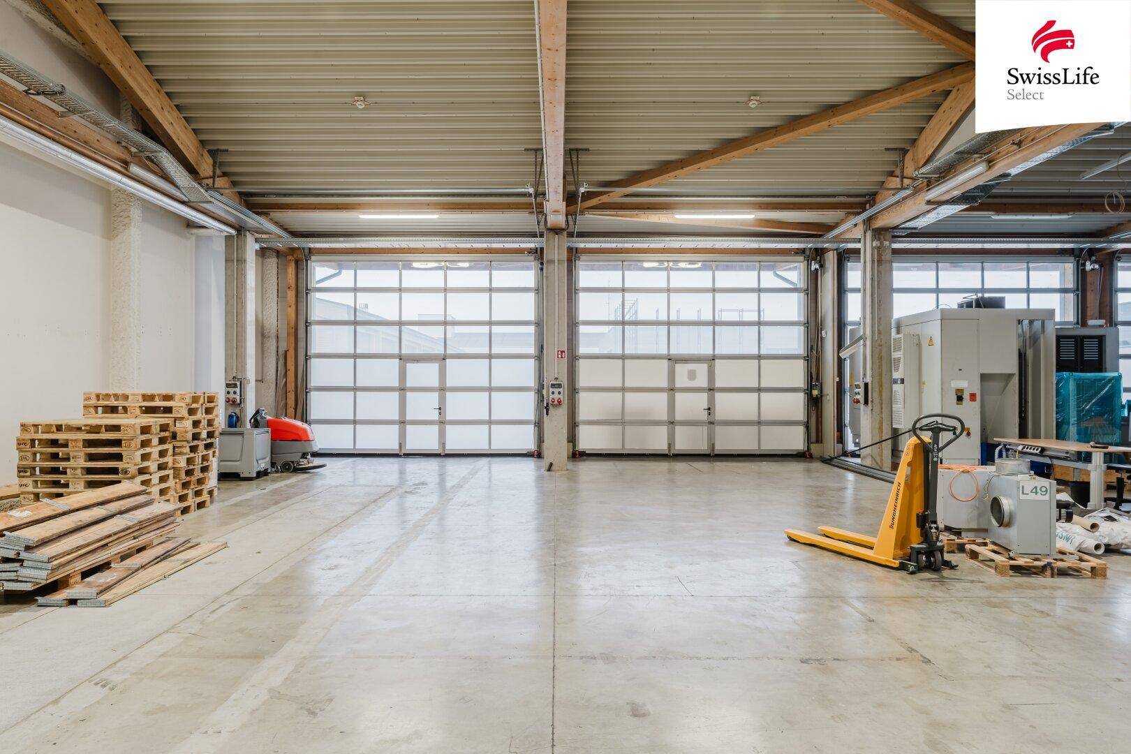 Helle Lagerhalle mit zwei großen Rolltoren und Betonboden, ideal für Anlieferung und Warenausgang.