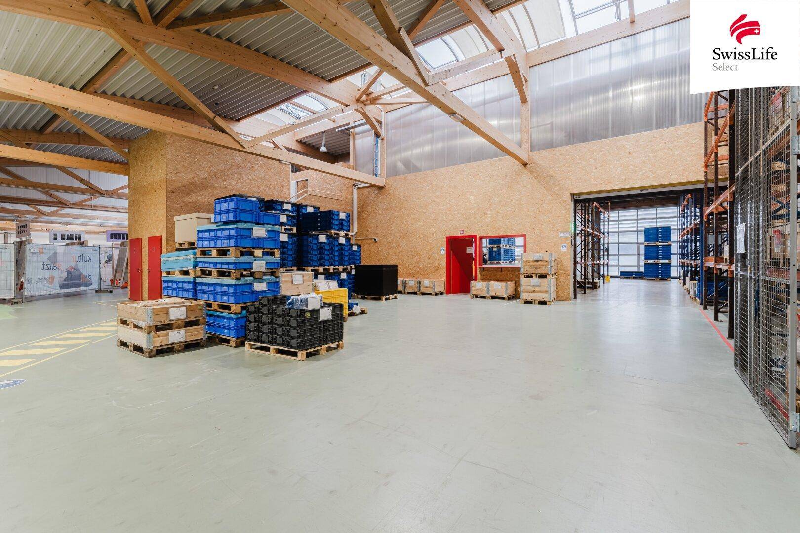 Lagerhalle mit hohen Regalen, Holzbalken und Oberlichtern, bietet viel Stauraum und Tageslicht.
