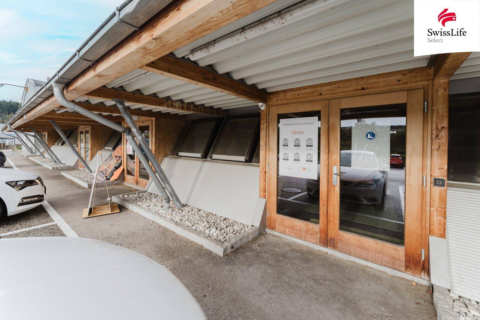 Moderner Gebäudeeingang mit Holztüren, großen Fenstern und Vordach, bietet einen einladenden Zugang.