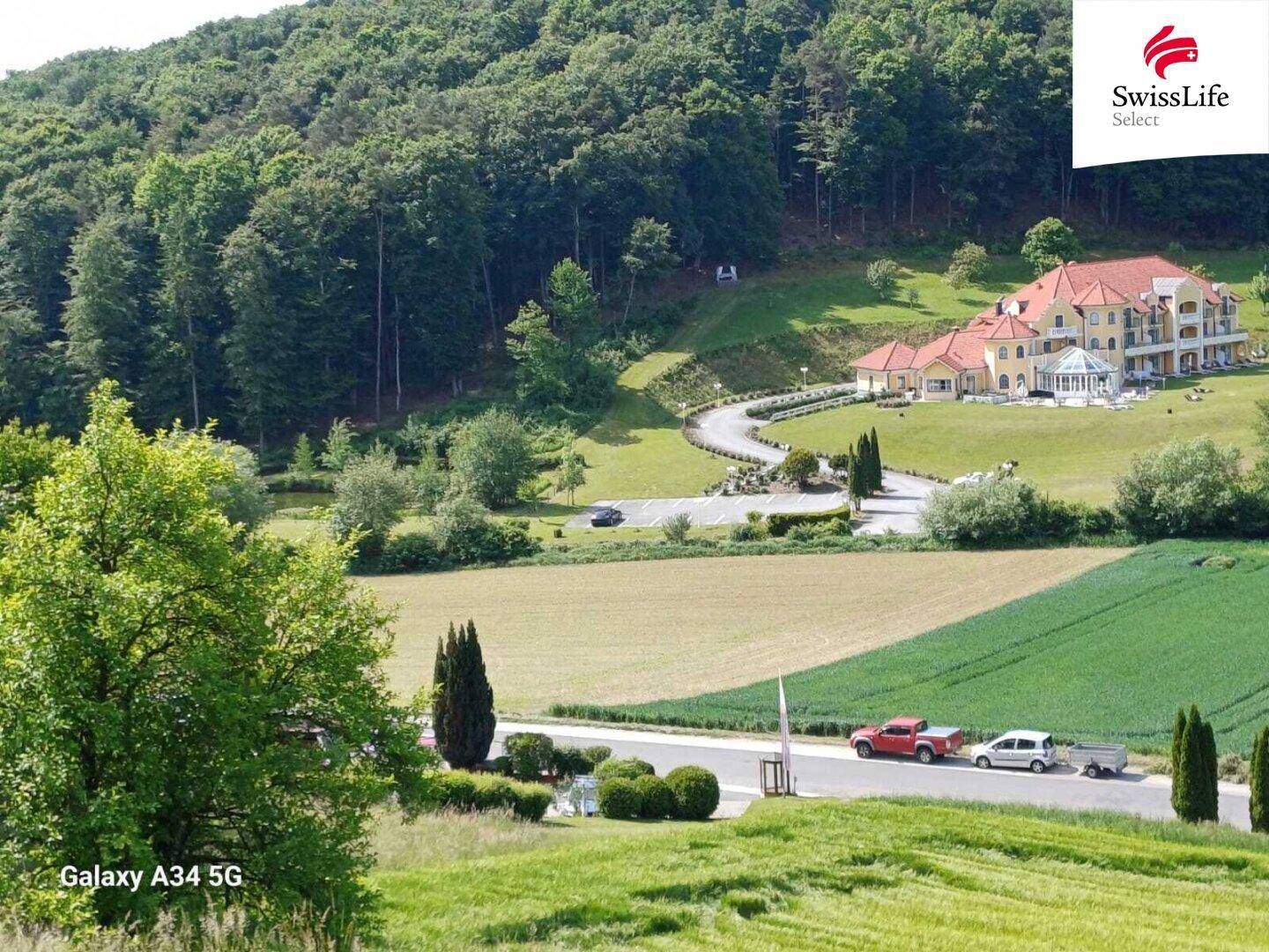 Panoramablick auf ein großes Anwesen, umgeben von grünen Hügeln und landwirtschaftlichen Flächen.
