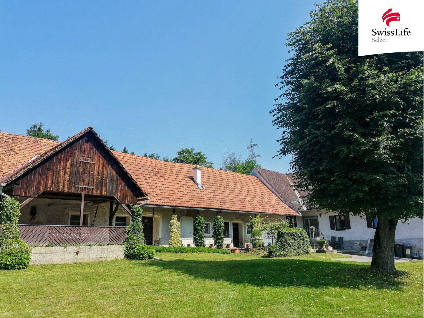 Historischer Bauernhof mit traditioneller Architektur und weitläufigen Grünflächen unter blauem Himmel.