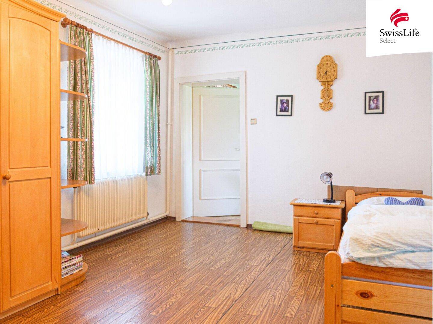 Helles Schlafzimmer mit Holzboden, Einzelbett und traditionellem Holzschrank.
