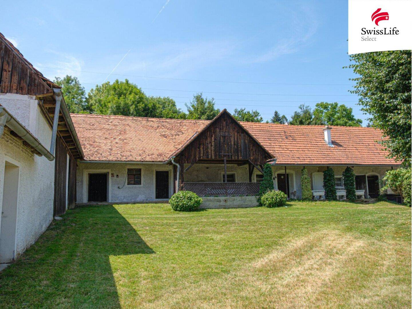 Ehemaliger Bauernhof mit großem Innenhof und viel Grünfläche unter blauem Himmel.