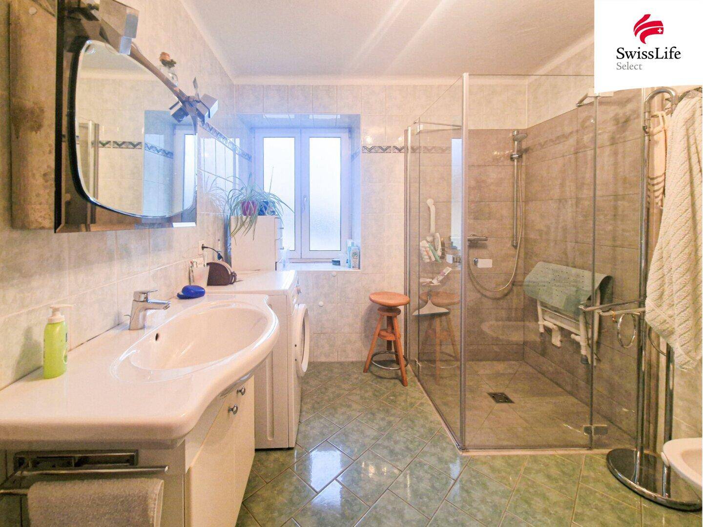Helles Badezimmer mit Dusche, Waschbecken und Fenster, ausgestattet mit grünen Fliesen.