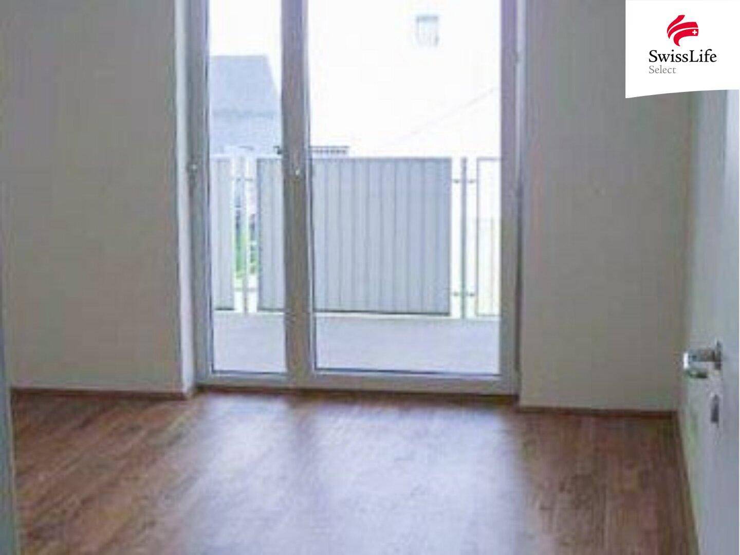 Heller Innenraum mit Holzboden und großem Fenster mit Zugang zu einem Balkon.