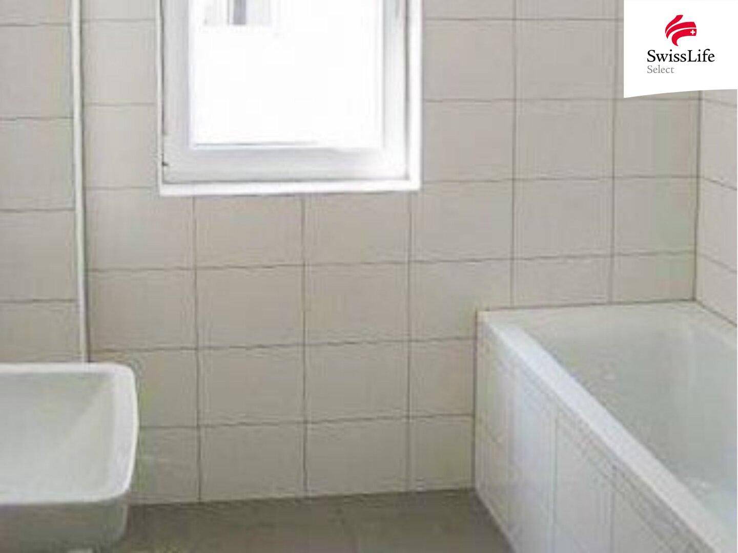 Badezimmer mit weißen Fliesen, Badewanne und einem Fenster für Tageslicht.