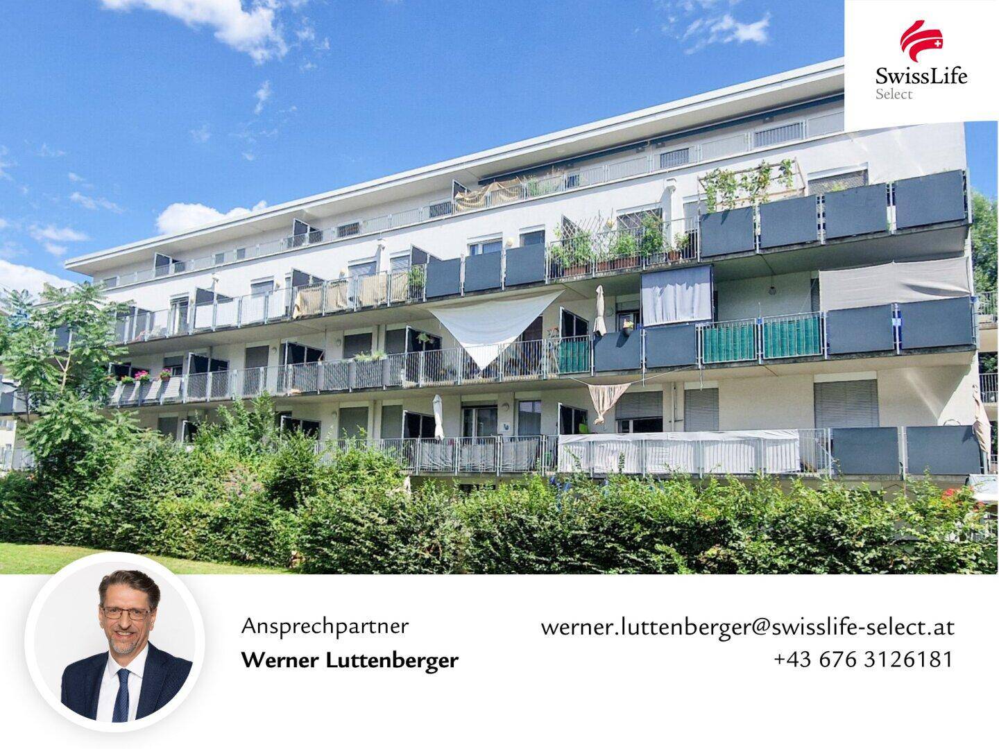 Mehrfamilienhaus mit vielen Balkonen und grüner Bepflanzung im Vordergrund.