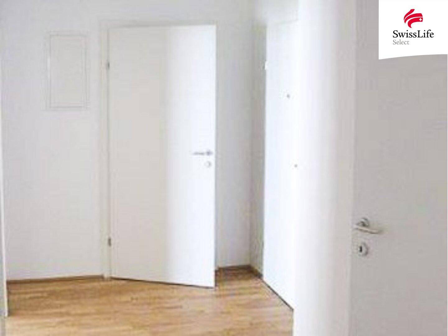 Heller Flur mit Holzboden und weißen Türen, der zu weiteren Räumen führt.