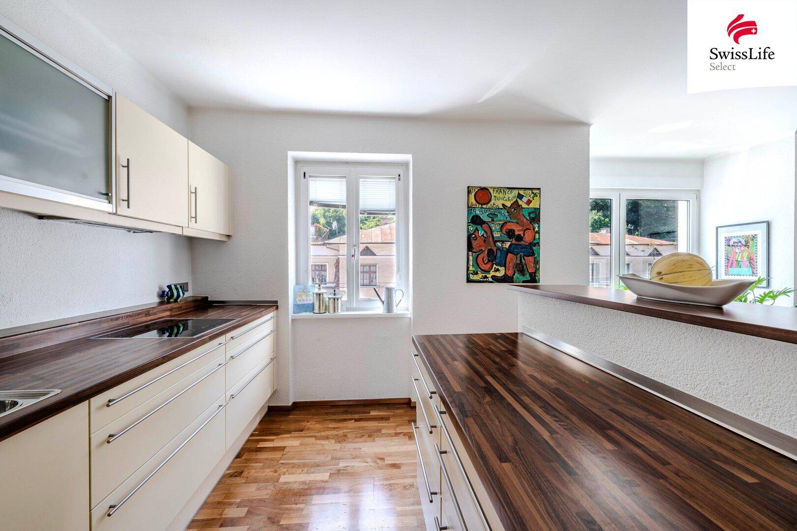 Moderne Küche mit beigen Schränken, dunklen Holzarbeitsplatten und einem Fenster.