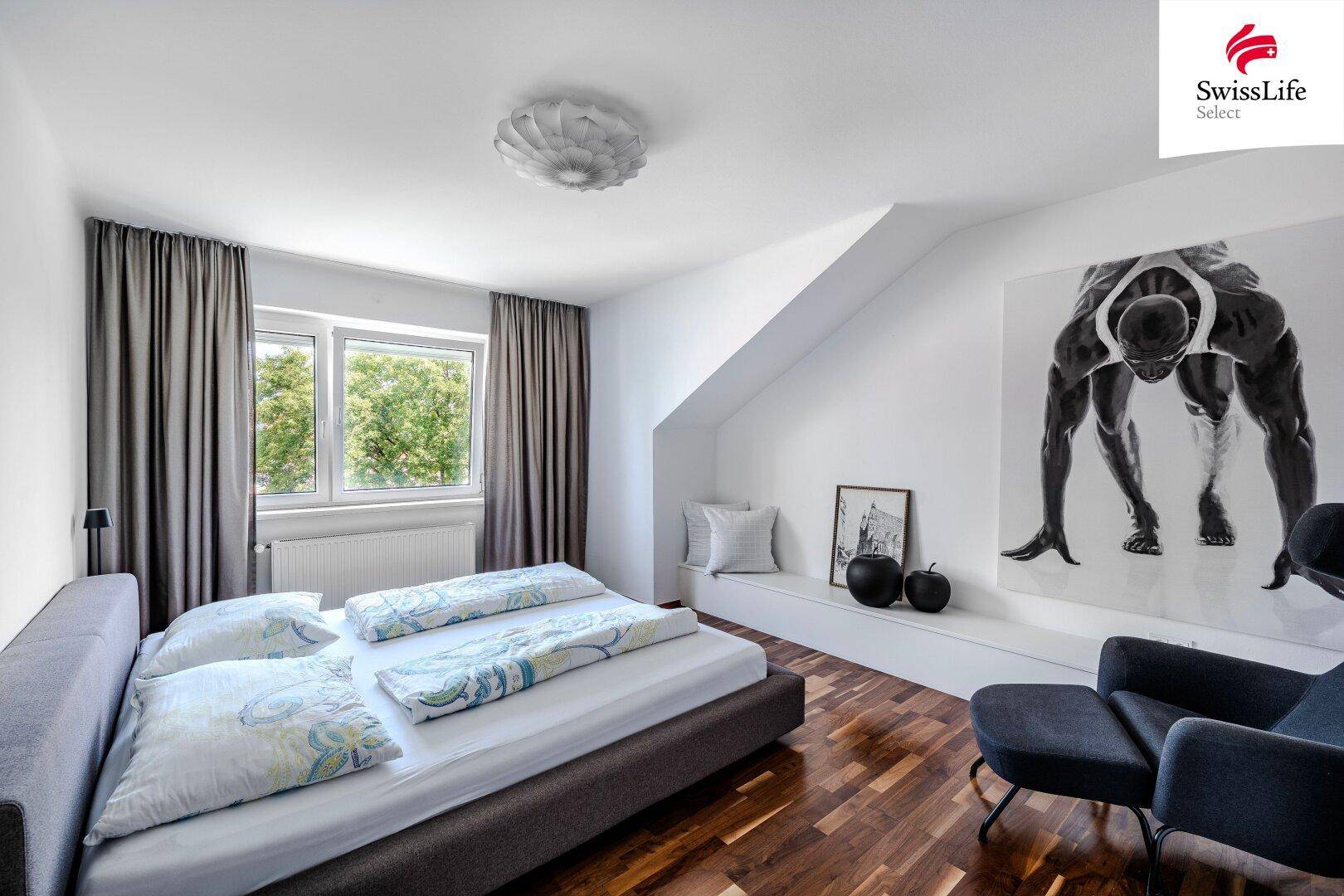 Helles Schlafzimmer mit Holzboden, Dachschräge, großem Fenster und Blick ins Grüne.