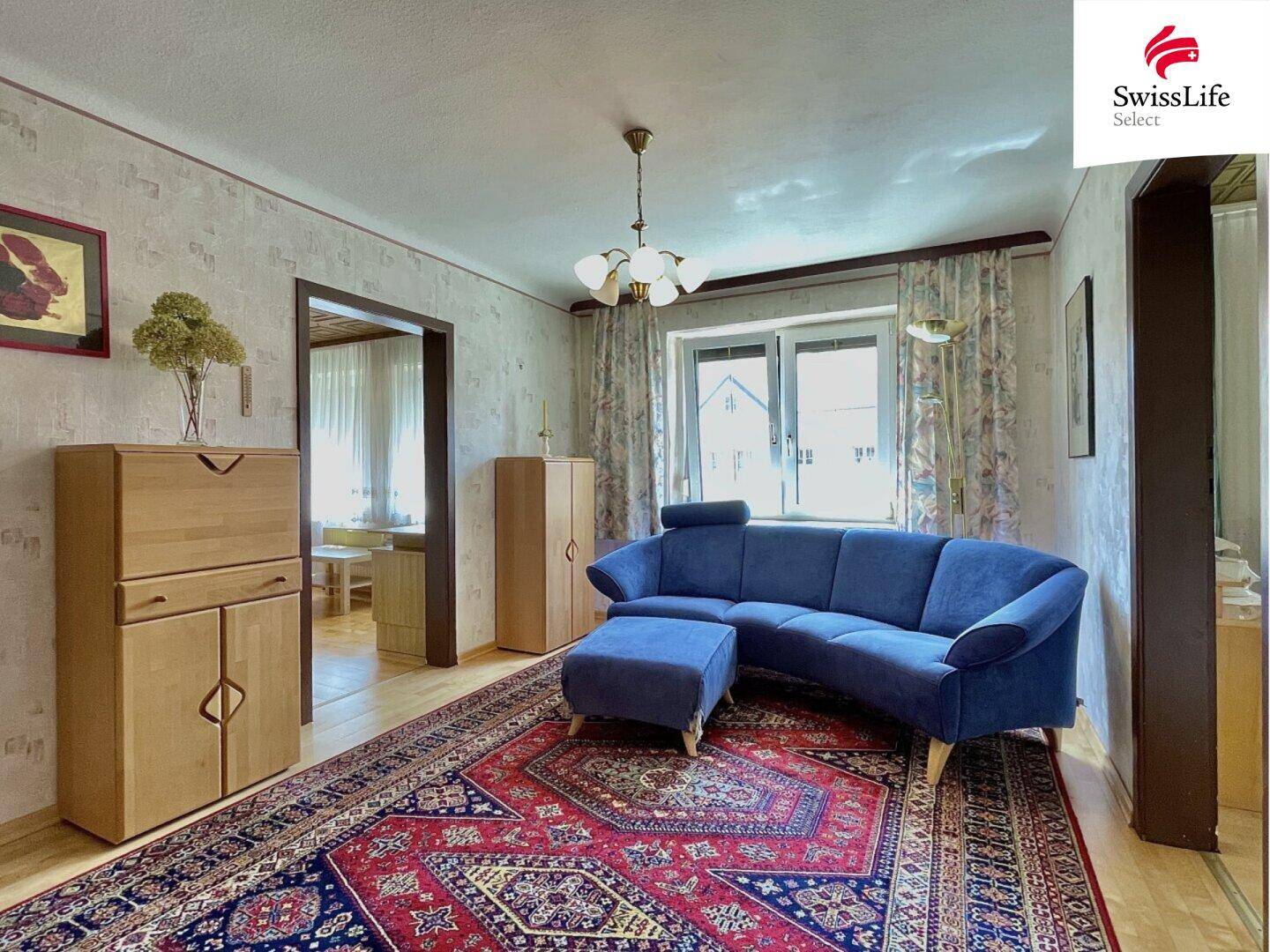 Geräumiges Wohnzimmer mit blauem Sofa, gemustertem Teppich und Holzmöbeln, bietet viel Platz.