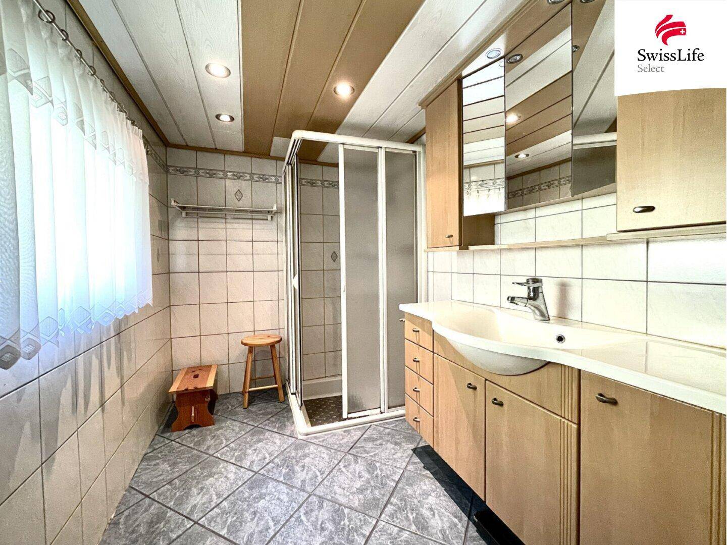 Funktionales Badezimmer mit Duschkabine, Einzelwaschbecken und hellen Fliesen an Wänden und Boden.