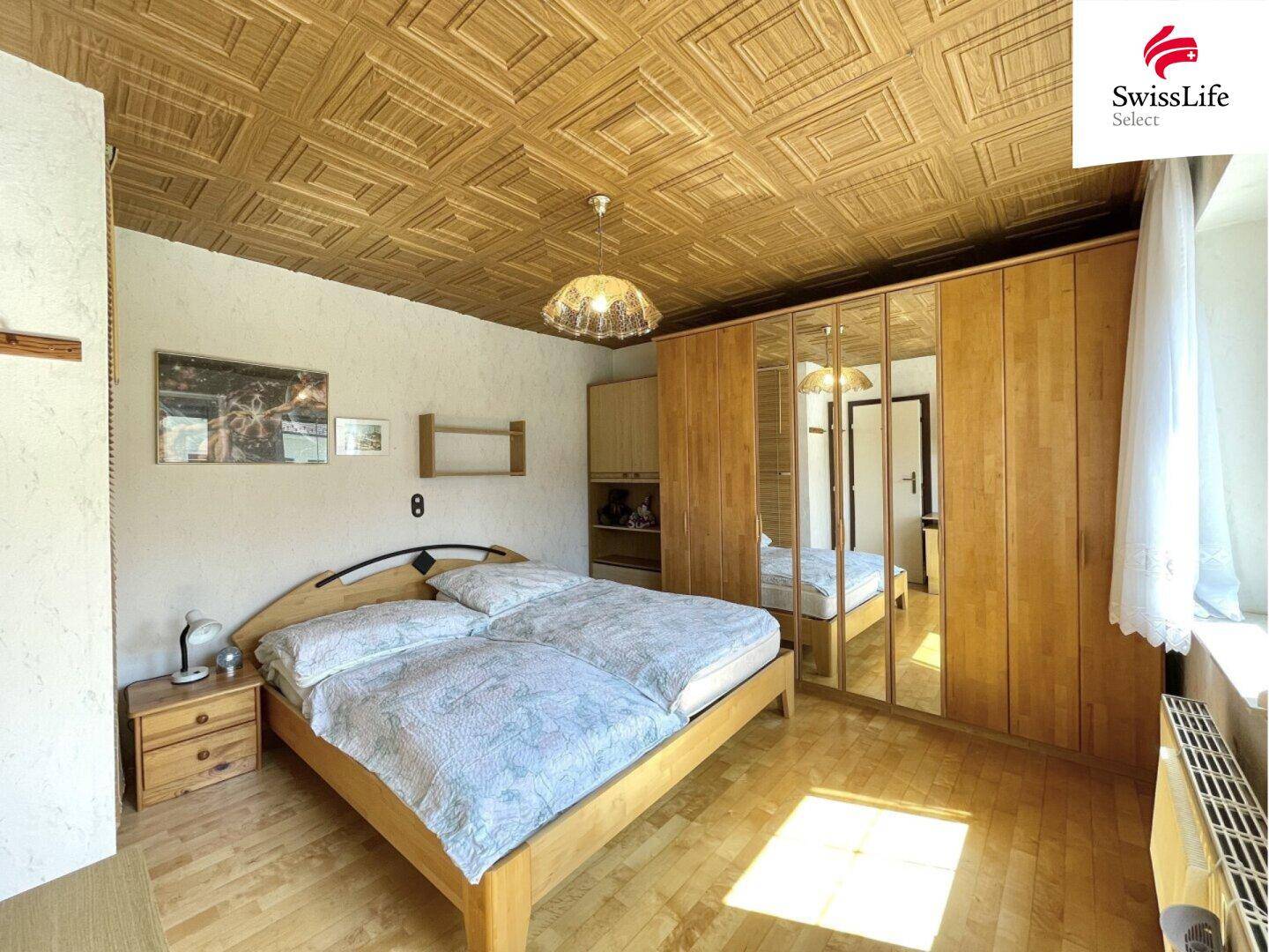Helles Schlafzimmer mit Doppelbett, großem Spiegelschrank und charakteristischer Holzdecke.