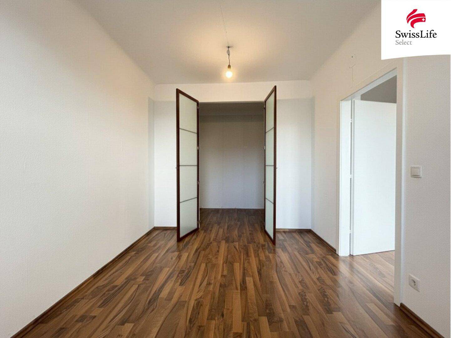 Helles Zimmer mit Holzboden und offenen Türen, das vielseitig genutzt werden kann.