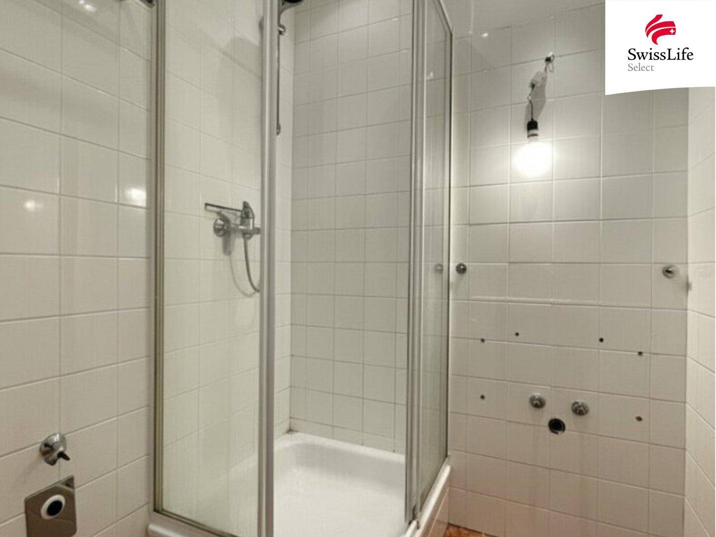 Badezimmer mit Duschkabine und weißen Fliesen, das eine Renovierung benötigt.