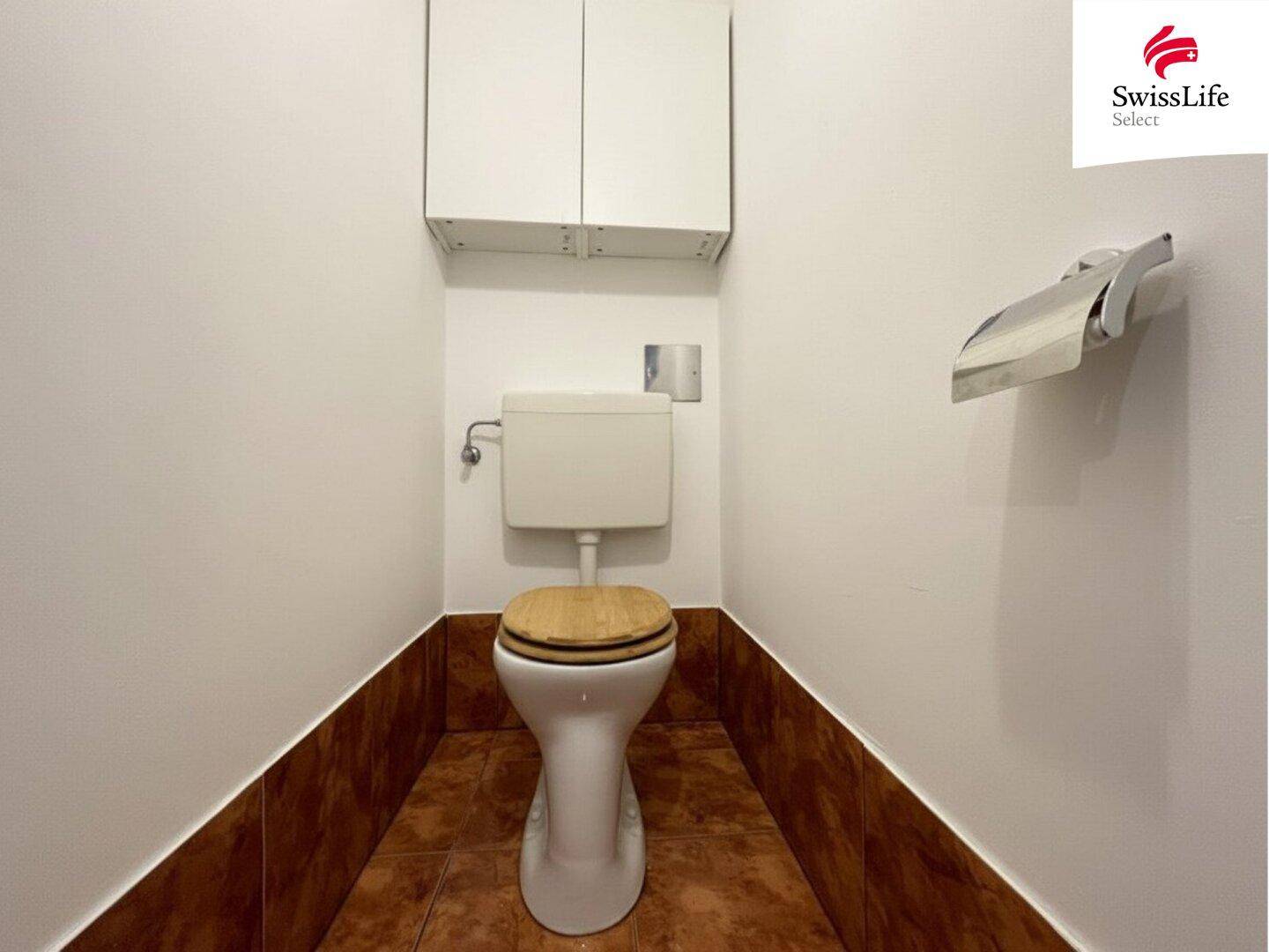 Separate Toilette mit braunen Fliesen und einem kleinen Hängeschrank.