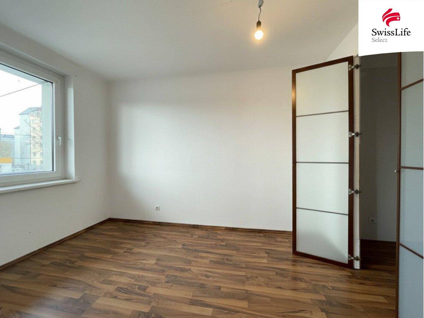Leeres Zimmer mit Holzfußboden und großem Fenster, bereit zur individuellen Gestaltung.