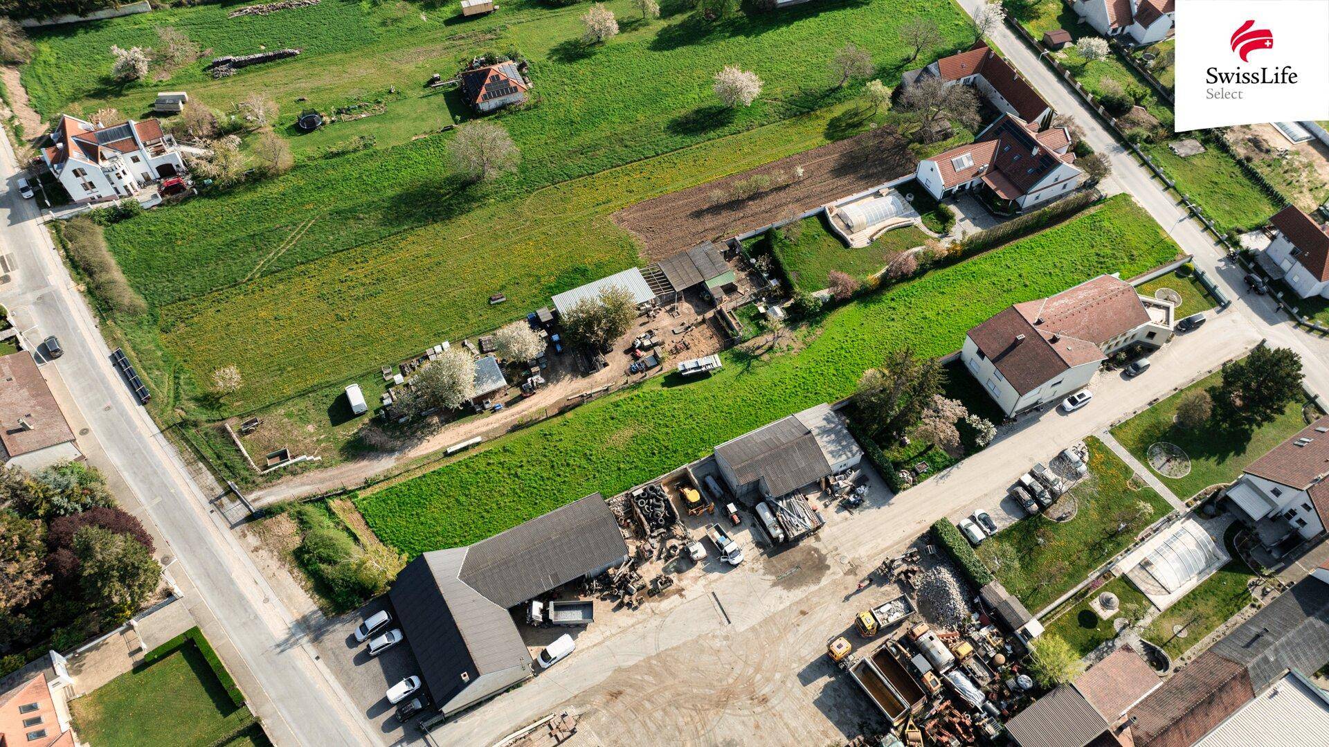 Luftaufnahme eines grünen Baugrundstücks, umgeben von Wohngebäuden und landwirtschaftlichen Flächen.