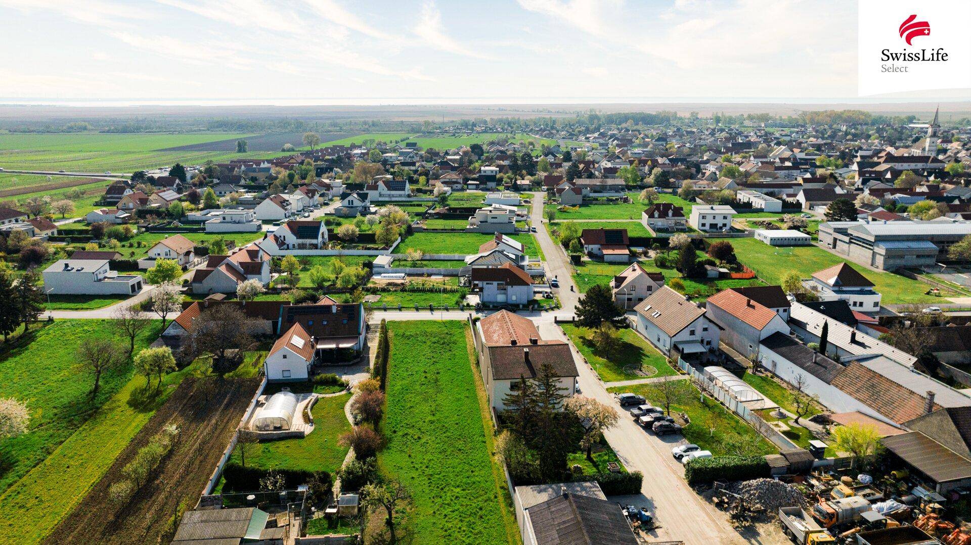 Weitläufige Luftaufnahme einer ländlichen Siedlung mit grünen Grundstücken und weitem Horizont.