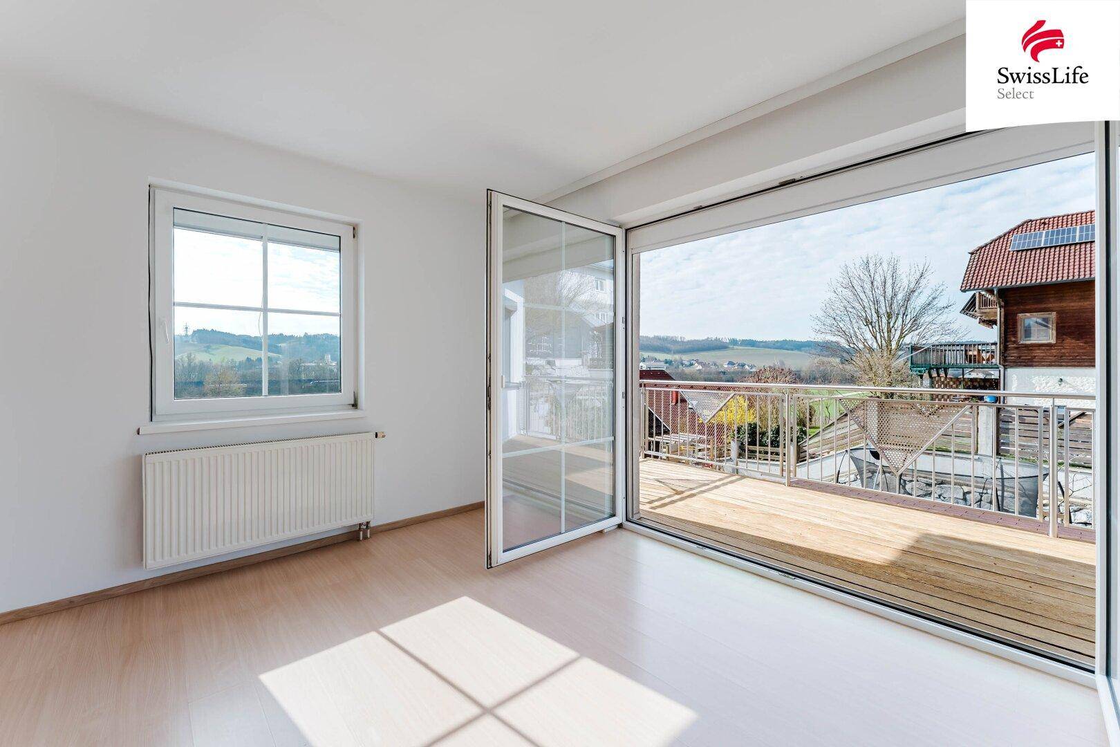 Helles Zimmer mit Holzboden und großem Zugang zu einem Balkon mit Weitblick.