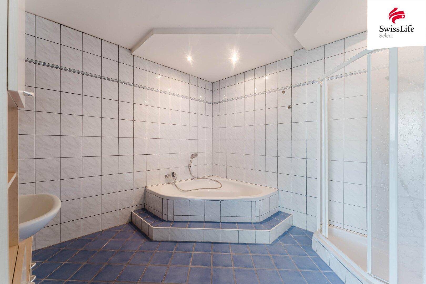 Badezimmer mit Eckbadewanne, Duschkabine und blauen Fliesen.