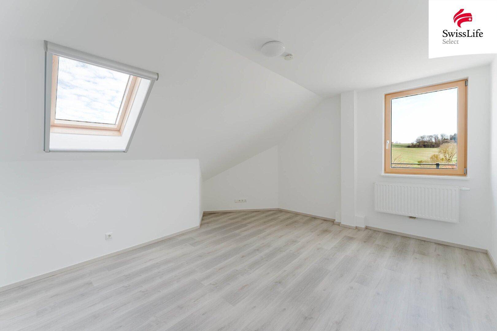 Helles Dachzimmer mit Schrägdecke, Dachfenster und Laminatboden.