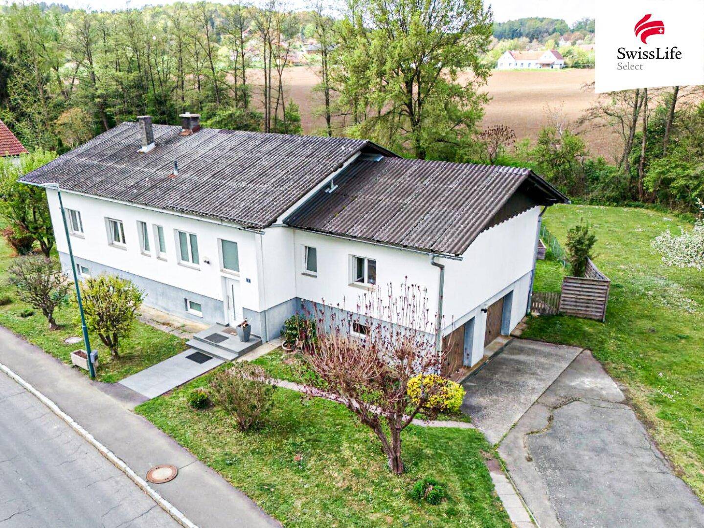 Ansicht des Einfamilienhauses von der Straßenseite mit Garage, Auffahrt und ländlicher Umgebung.