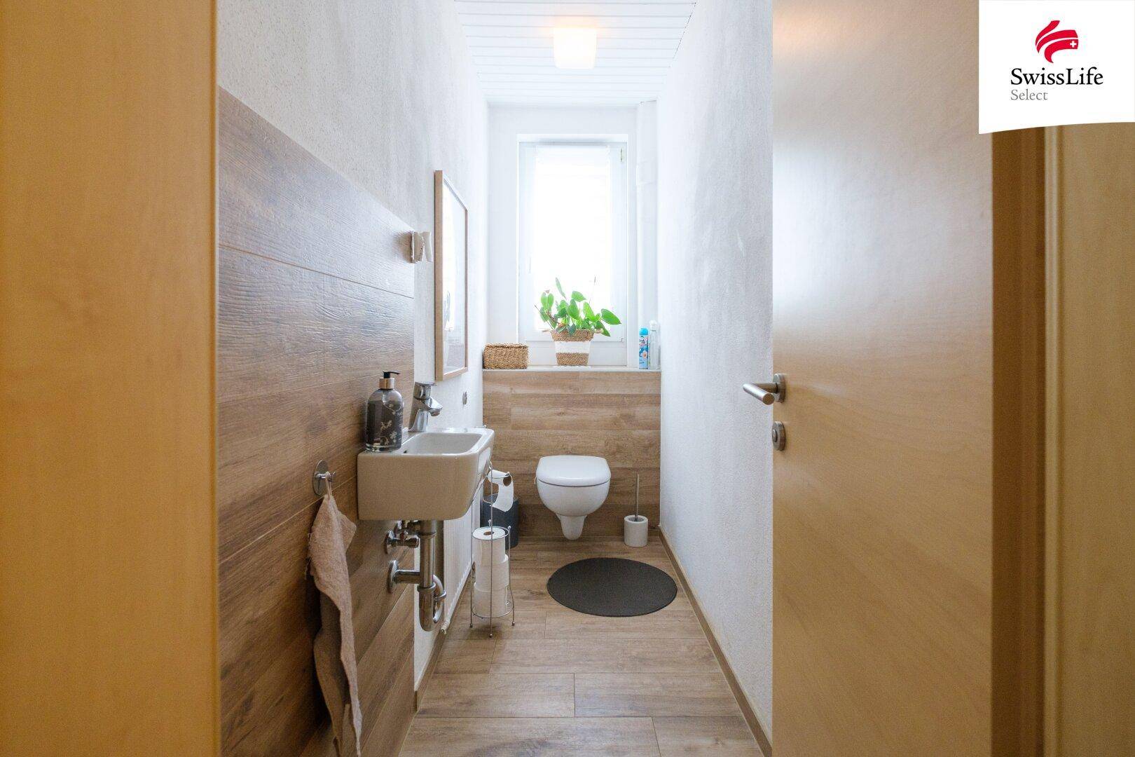 Gepflegtes Gäste-WC mit kleinem Waschbecken, Toilette und Fenster, das für Helligkeit sorgt.