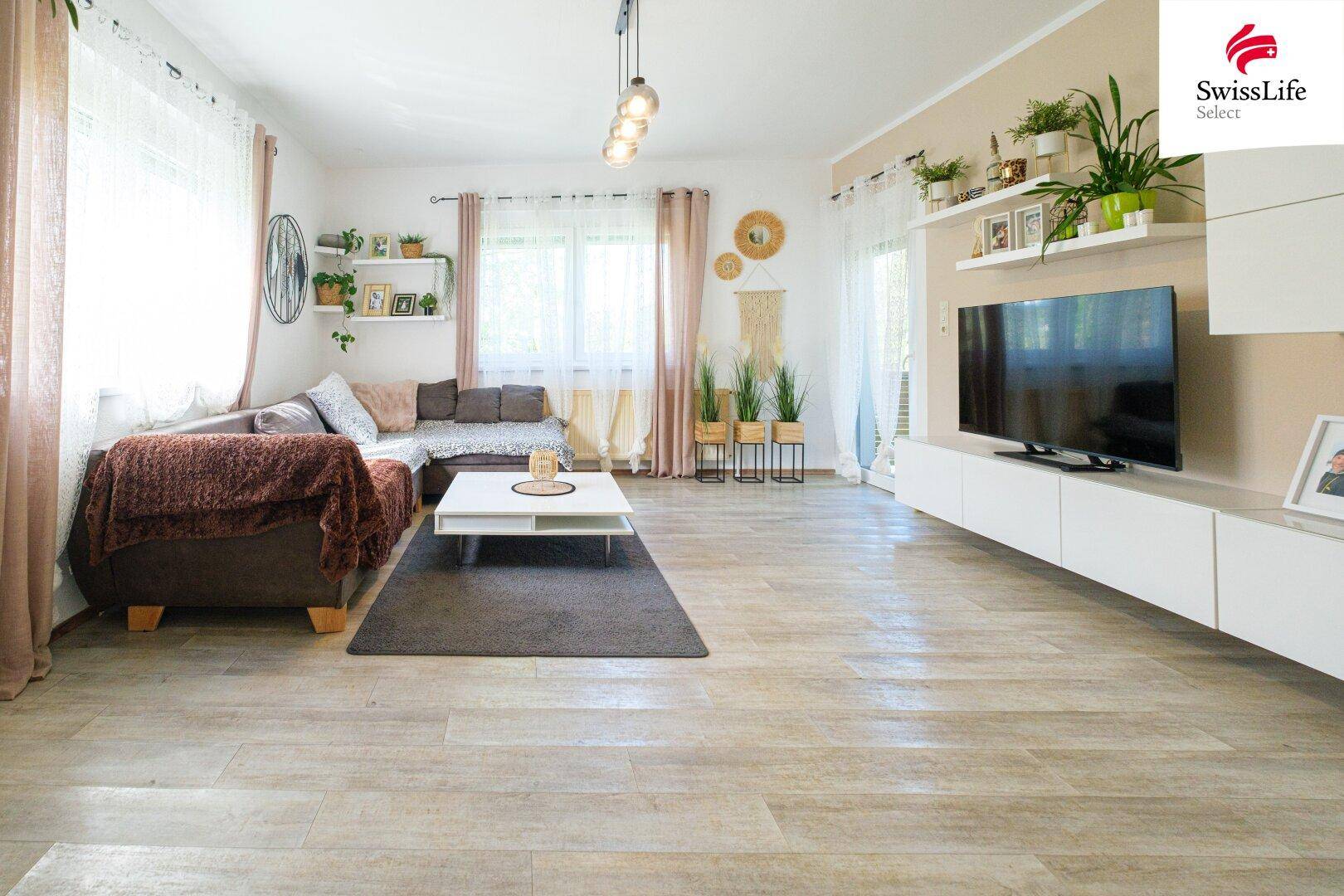 Helles Wohnzimmer mit beigem Sofa, modernem TV-Möbel und vielen Pflanzen, das zum Entspannen einlädt.