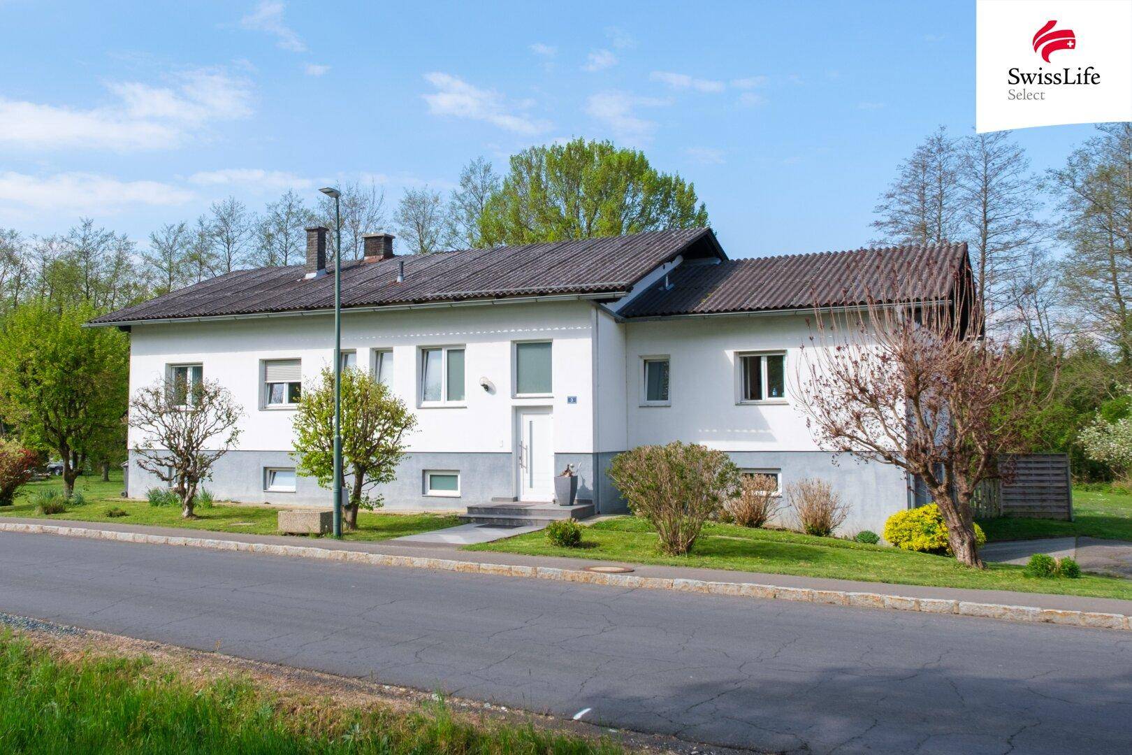 Frontansicht des Hauses von der Straße aus, umgeben von gepflegter Vegetation und blauem Himmel.