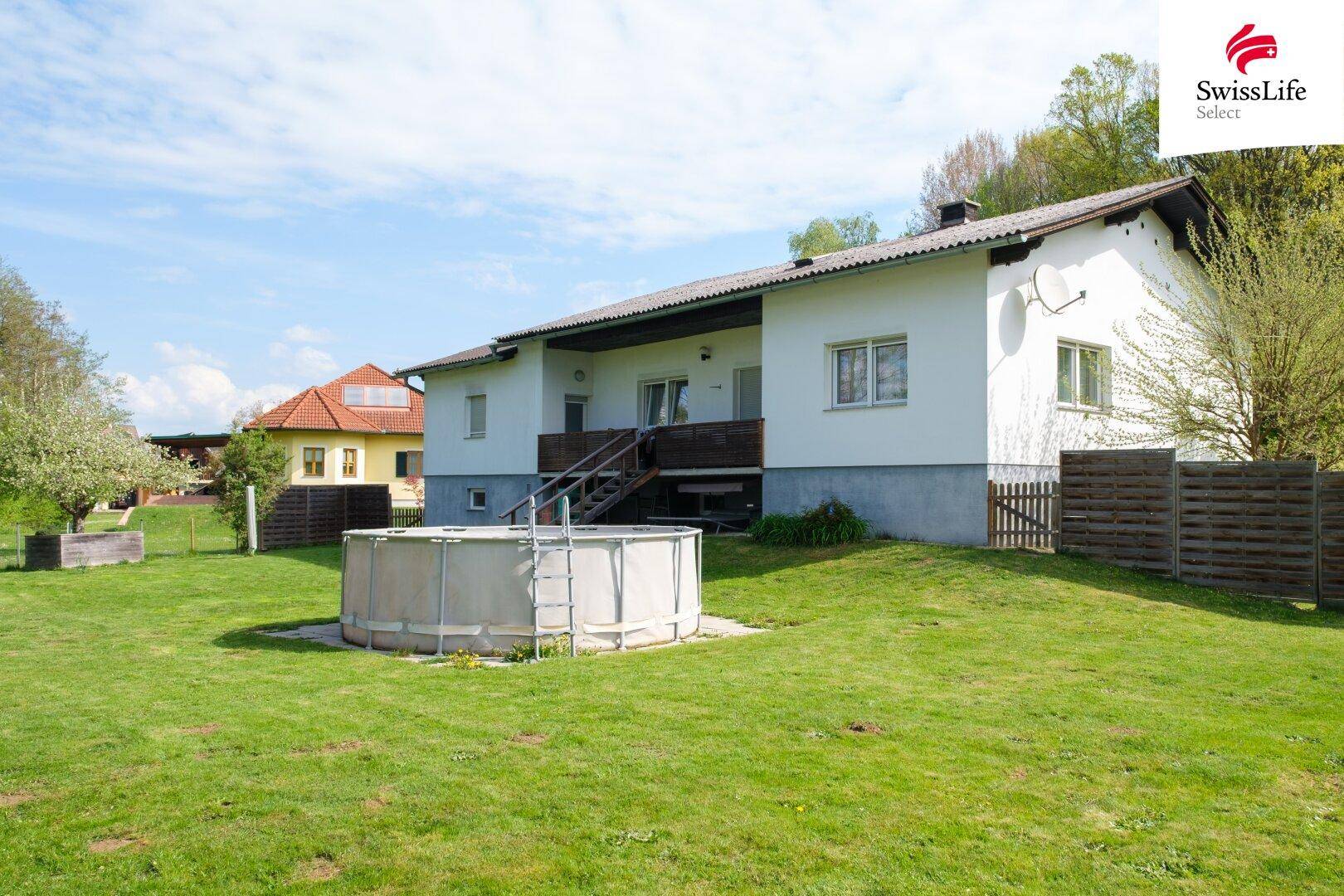 Rückseite des Hauses mit großem Garten und einem Aufstellpool, umgeben von viel Grün.