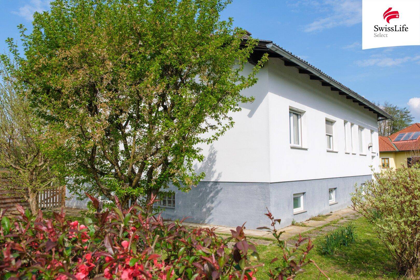 Seitenansicht des Hauses mit üppigen Bäumen und Sträuchern, die eine natürliche Umgebung schaffen.