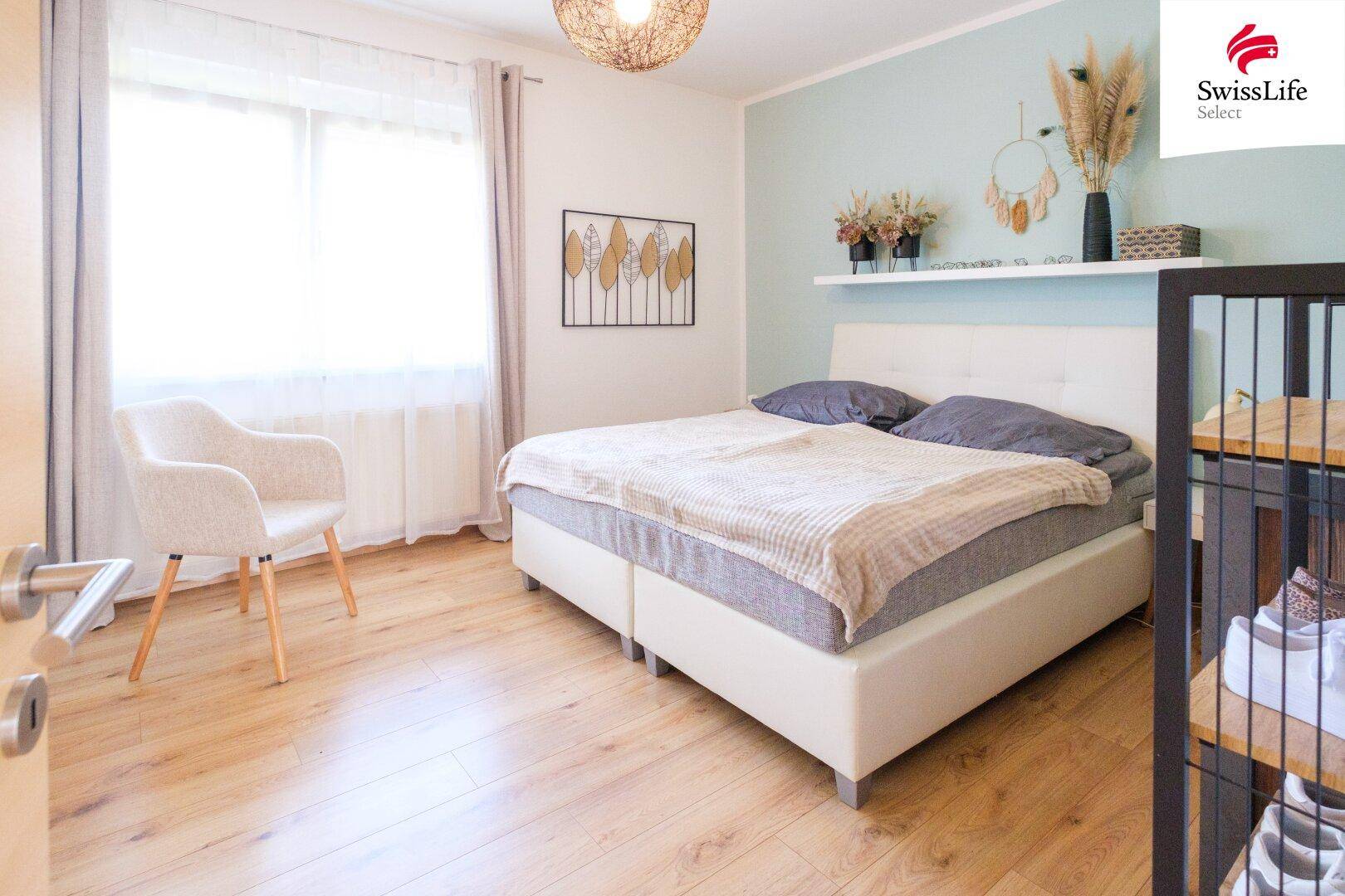 Helles Schlafzimmer mit Doppelbett, hellgrüner Akzentwand und Holzboden, das eine ruhige Atmosphäre schafft.