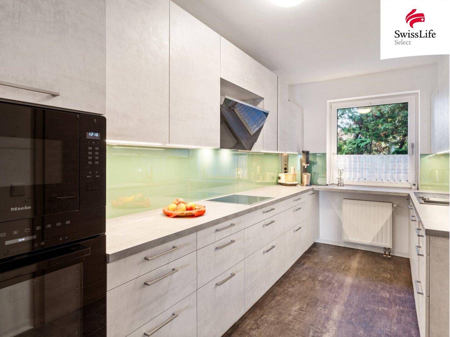 Moderne Einbauküche mit Miele-Geräten, Induktionskochfeld und Fenster zum Garten.