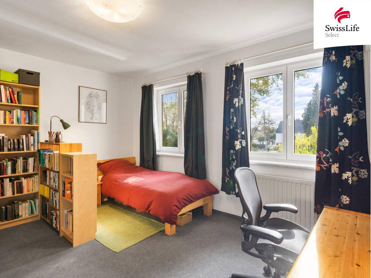 Gemütliches Schlafzimmer mit Teppichboden, Bücherregal und Blick ins Grüne.
