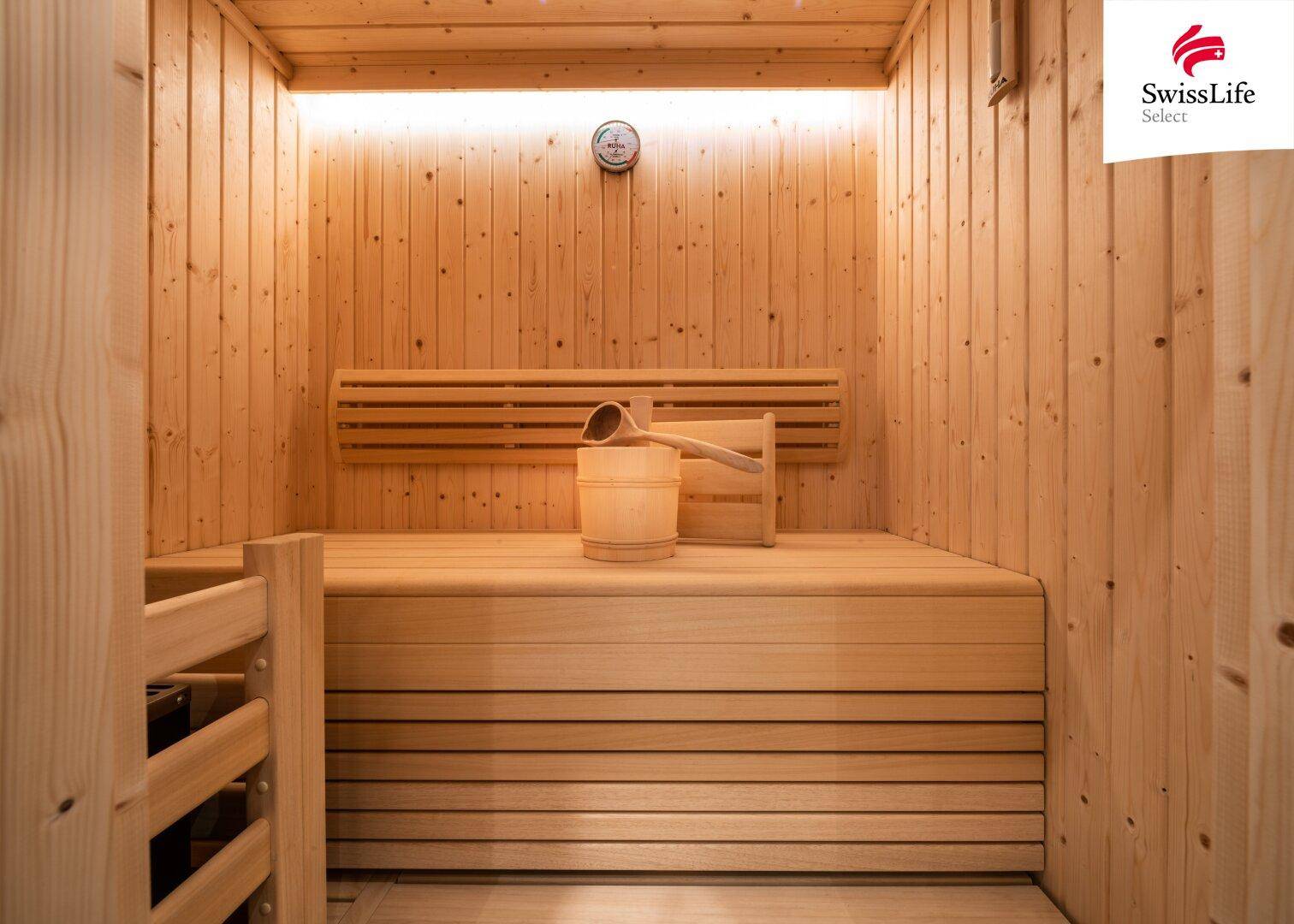 Moderne Holzsauna mit traditionellem Aufgusseimer und Sanduhr für Entspannung.