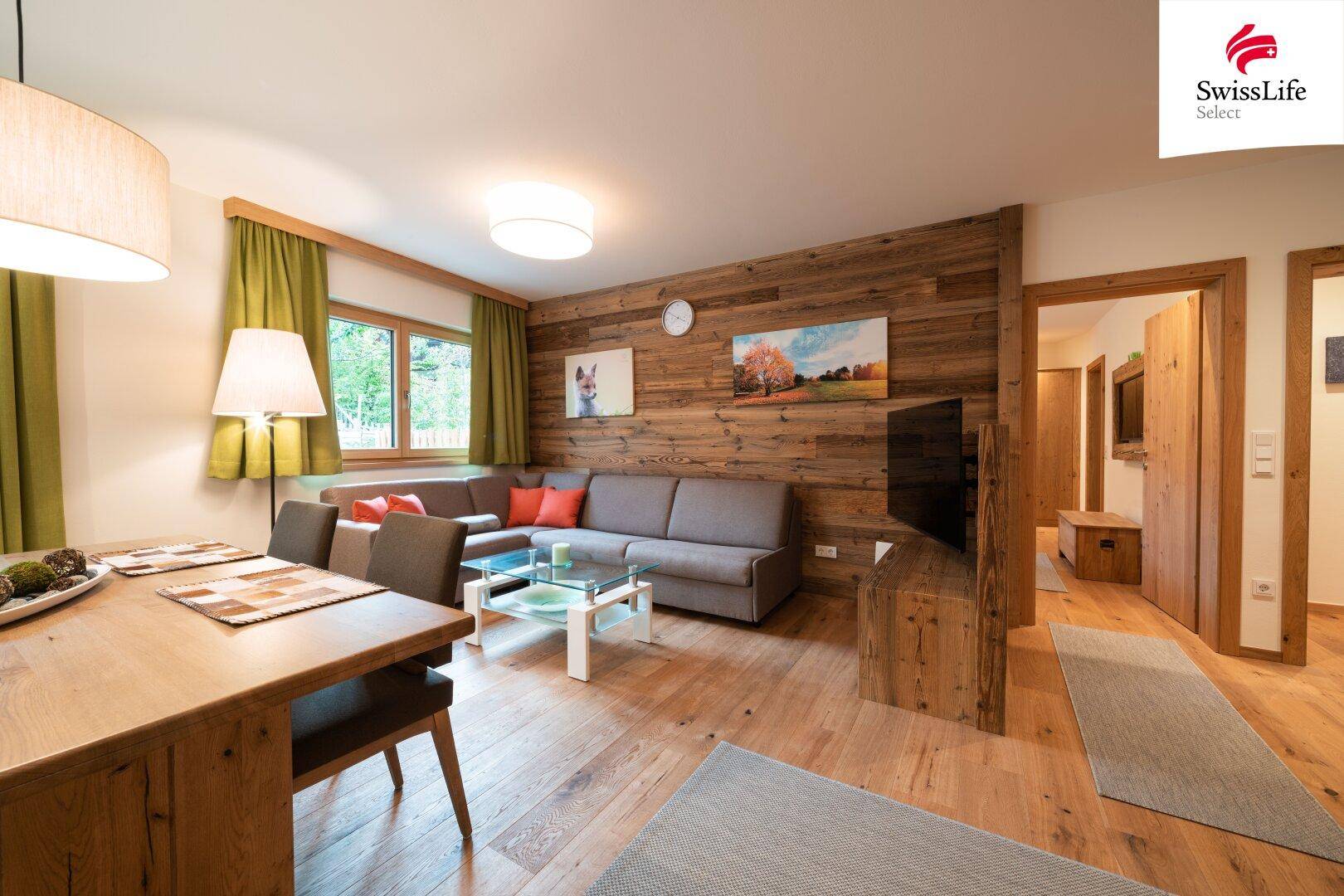 Gemütlicher Wohnbereich mit Holzwandverkleidung, Sofa und Zugang zu weiteren Räumen im alpinen Stil.