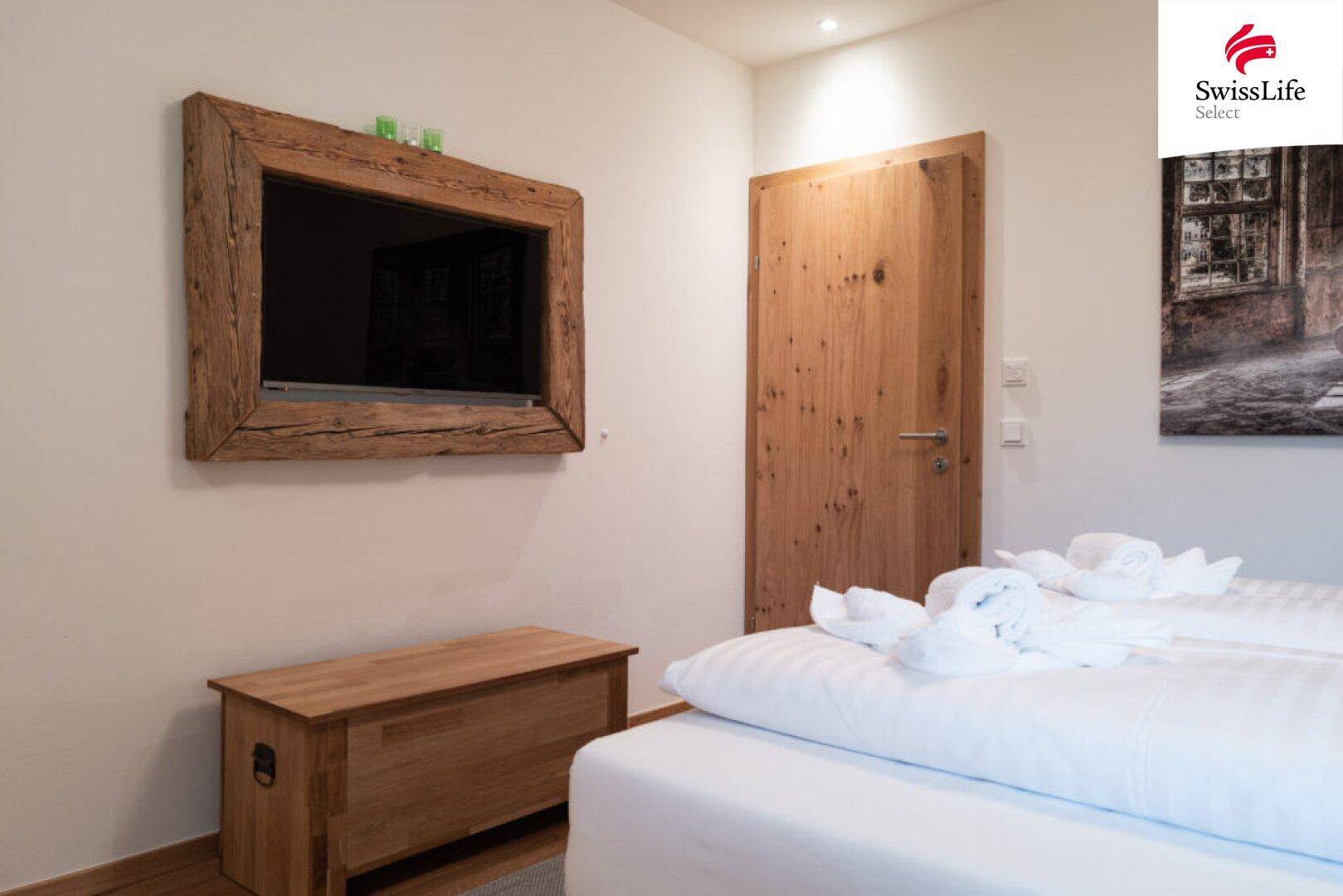 Schlafzimmer mit bequemen Betten, Holztür und einem Fernseher in rustikalem Holzrahmen.