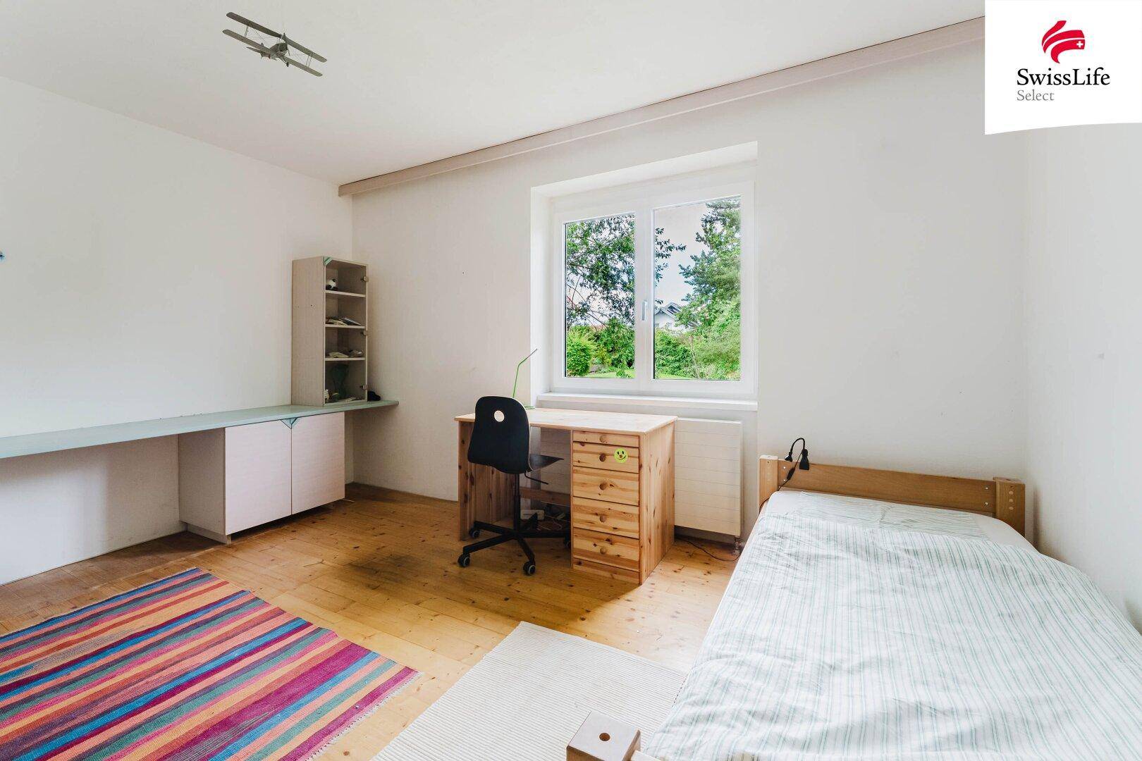 Helles Schlafzimmer mit Holzboden, Schreibtisch und Blick ins Grüne.