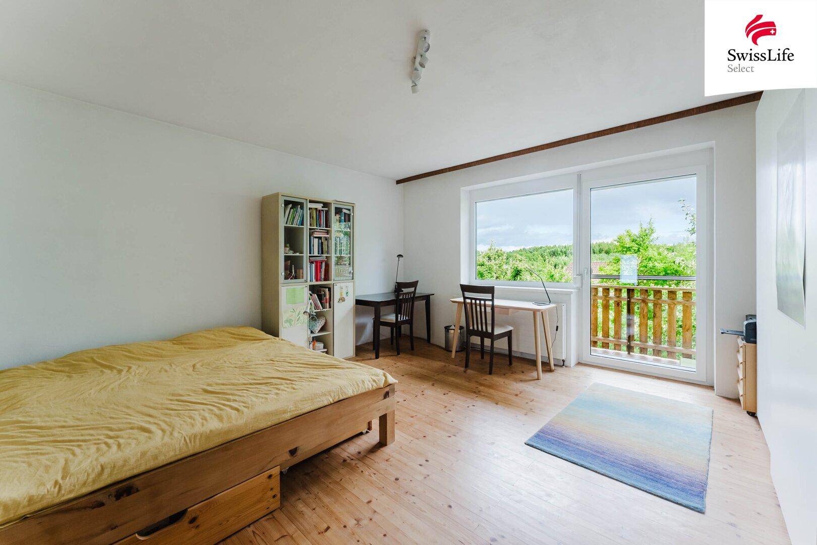 Geräumiges Schlafzimmer mit Holzboden, Schreibtisch und Zugang zum Balkon.