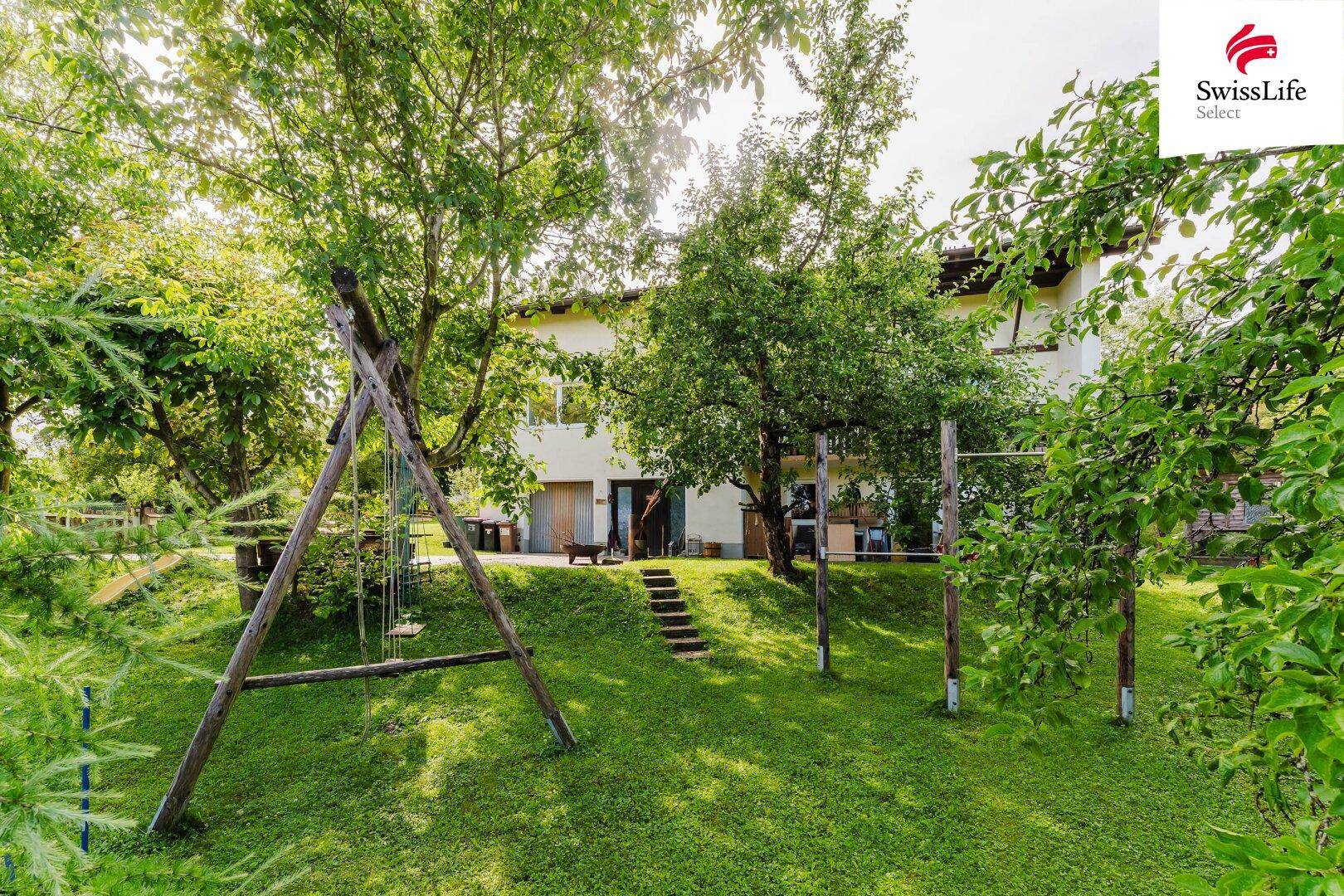 Großer Garten mit Rasenfläche, Obstbäumen und Schaukel für Kinder.